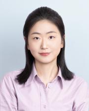 Young woman with dark hair wears a lilac colored shirt in front of a light blue background. 