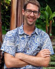 Photograph of Taylor Tappan wearing a blue and white shirt. Arms folded over his chest. Smiling. 